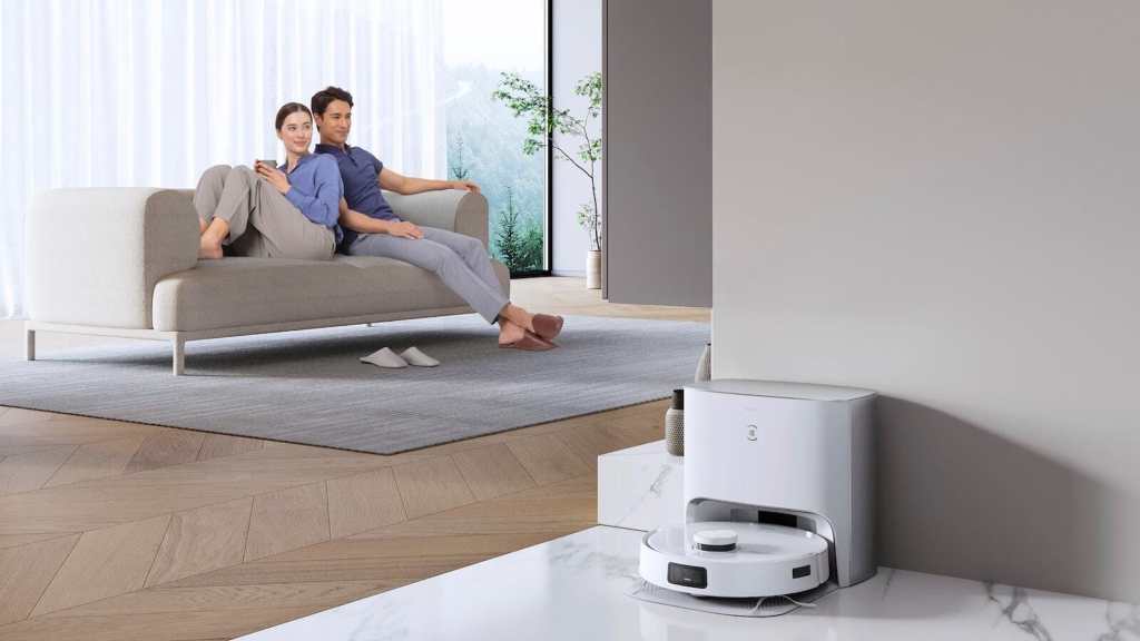 Couple relaxing on sofa with automatic robot vacuum cleaner docking in modern living room.